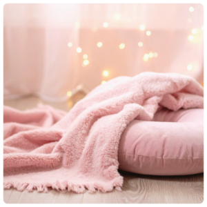 A pink pillow and blanket with fairy lights in the background.