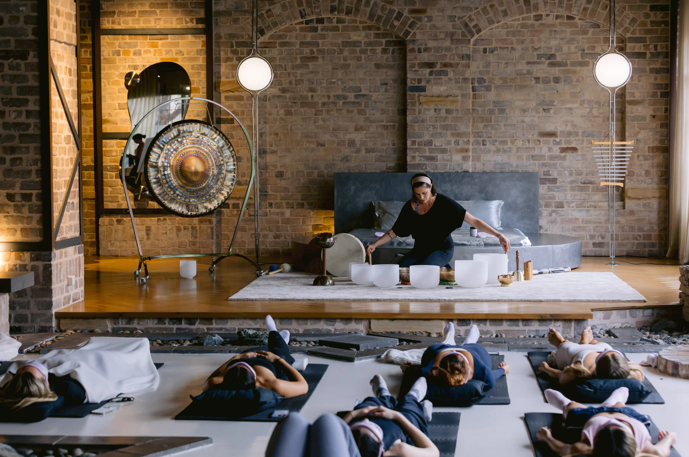Natalie Grace leading a sound bath with guests reclining in front of singing bowls and a gong